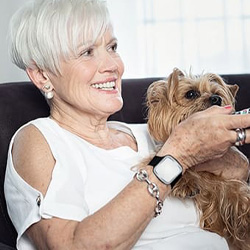 Une femme senior avec un détecteur de chute de téléassistance qui regarde la télévision en compagnie de son chien