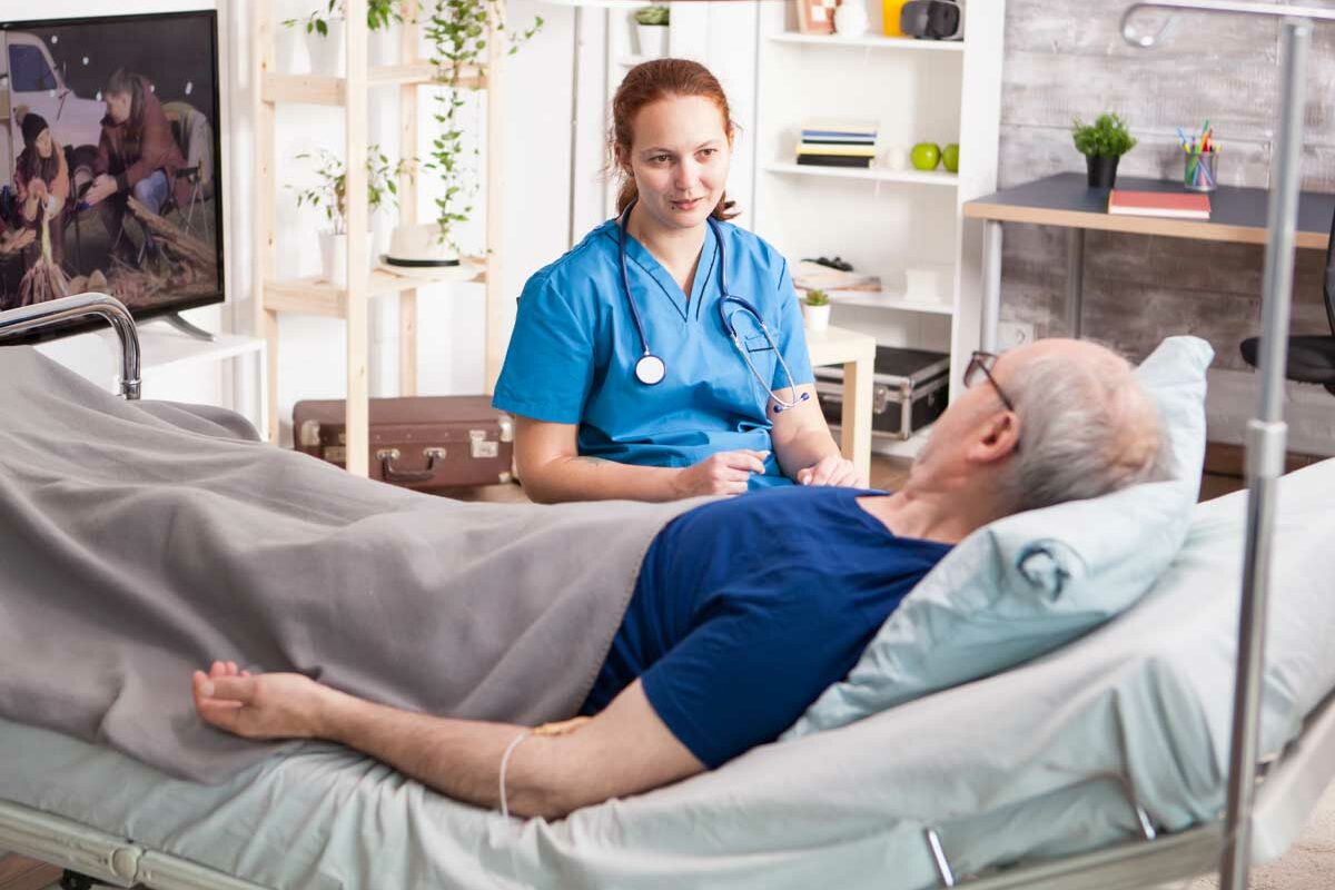 Un homme senior bénéficiant de l'ARDH avec son médecin à domicile, dans son lit médicalisé