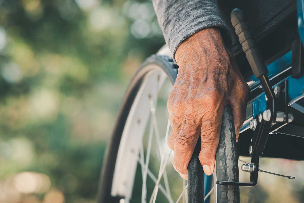 La main d'un vieil homme sur un fauteuil roulant, bénéficiaire d'une pension d'invalidité